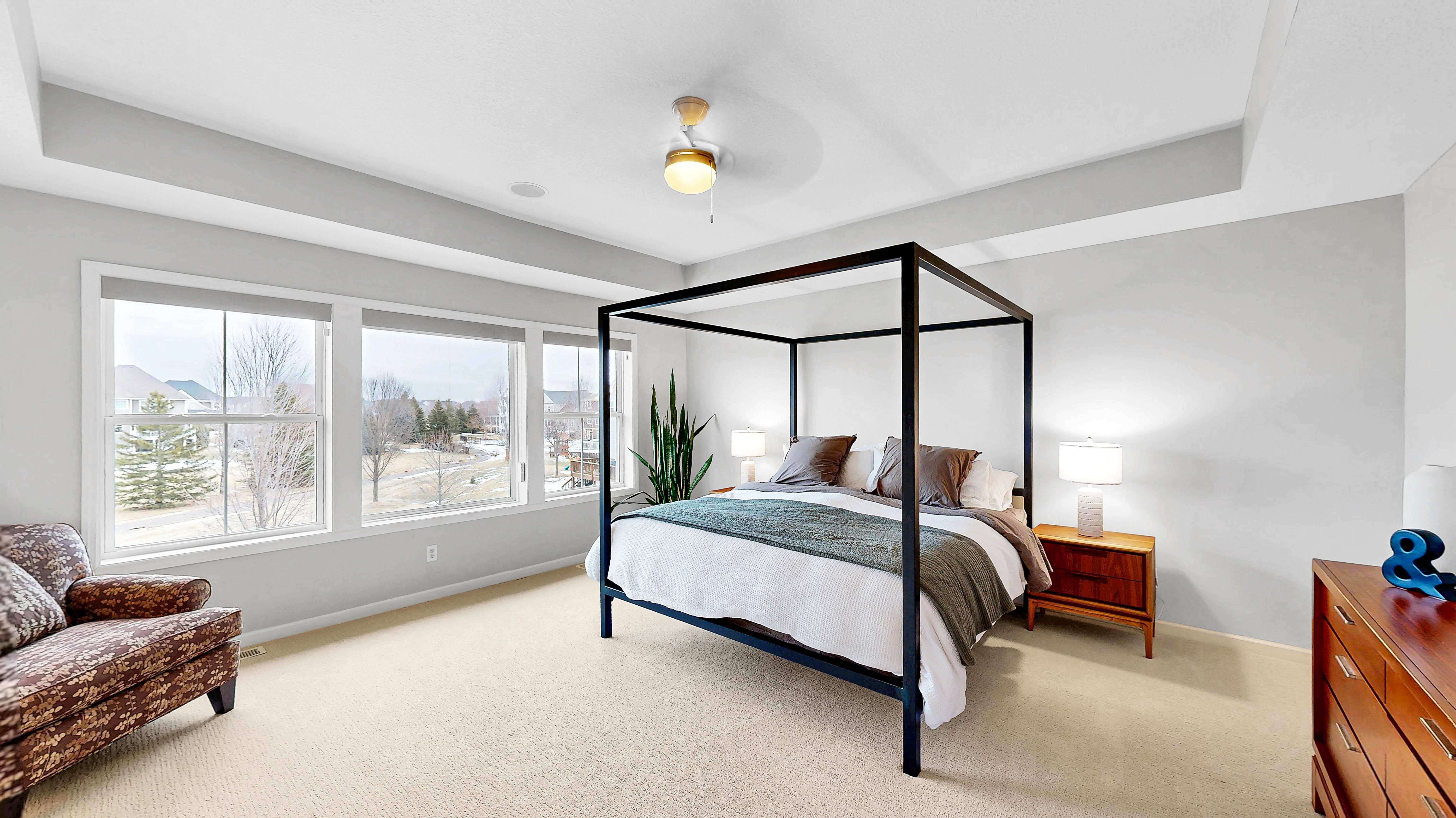 Spacious primary bedroom with tray ceiling, canopy bed, and bay windows
